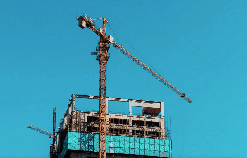 A crane is perched atop a tall building with vibrant blue sky behind it