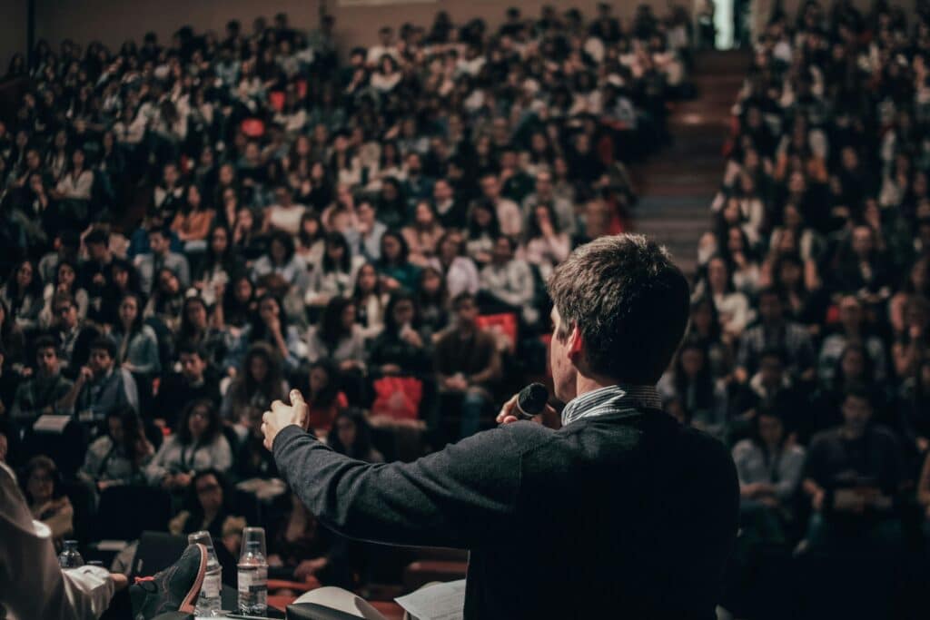 A man is speaking to a large, seated crowd
